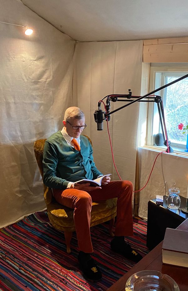 En man sitter i en fåtölj och läser en bok och har två mikrofoner att prata i, vacker inredning, mannen heter Anders Wallin och är hypnotisör och författare